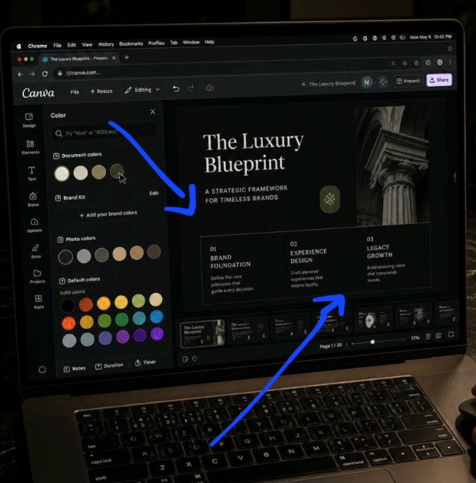 A first-person POV photograph of a creative strategist sitting at a modern dark desk, using a laptop screen running Chrome to build a moody dark-mode asset layout inside Canva